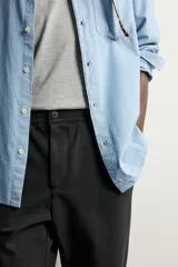 Pantalón negro confeccionado en mezcla de algodón, con cintura elástica, bolsillos frontales y cierre con cremallera y botón.