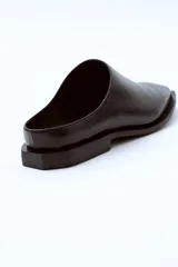 Mocasín negro de cuero con punta cuadrada y talón descubierto.