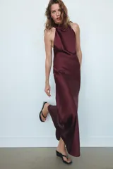 Vestido largo de satén en color bordó, con cuello halter y detalle de lazada en el cuello. Presenta un diseño fluido con espalda descubierta.