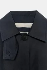 Parka de cuello alto con trabilla y manga larga, color azul marino. Presenta bolsillos laterales ocultos en la costura y cintura ajustable con cordón. El cierre frontal es con botones ocultos por solapa.