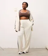 Pantalón deportivo de corte oversized estilo college, confeccionado en microfibra color crema con rayas laterales contrastantes en color marrón. Presenta cintura fija, bolsillos funcionales y frisos frontales.