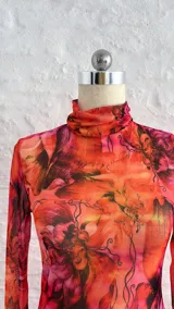 Vestido corto de microtul elastizado con estampado floral en tonos naranja, rosa y negro. Tiene cuello alto y mangas largas acampanadas.