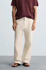 Pantalón de corte recto, color beige claro, con pliegues frontales y bolsillos de vivo en la parte trasera.
