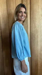 Camisa de jean celeste con cuello redondo, mangas abullonadas y puños elásticos. Cierre frontal con botones.