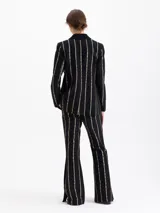 Pantalón negro de tiro alto con fit flare, confeccionado en jacquard con motivo de cadenas doradas que forman rayas verticales. Presenta tajos en los laterales del ruedo.