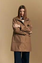 Pilot de largo medio color tostado, con capucha integrada, cierre frontal oculto y bolsillos aplicados con tapa. Presenta un diseño de líneas rectas y funcionales con un estilo urbano y atemporal.