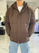 Campera puffer impermeable color beige con capucha desmontable con cordones negros, cierre frontal con cremallera y solapa con botones a presión.