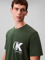 Remera de cuello redondo y manga corta, confeccionada en tejido de punto de algodón. Presenta un estampado frontal con el monograma de Calvin Klein y el logo de la marca en color blanco sobre un fondo verde oscuro.