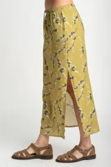 Falda midi color verde oliva con estampado de ramas en negro y blanco. Tiene corte evasé, cintura alta con cordón ajustable y abertura lateral.