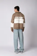 Buzo tipo polo de calce relajado con diseño de bloques de color en tonos marrón y blanco. Presenta cuello polo, cierre frontal parcial y logo estampado en el pecho. Confeccionado en tejido pesado con estructura.