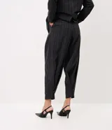 Pantalón de sastre de corte wide leg con diseño de rayas verticales, confeccionado en crepé color gris oscuro. Cuenta con tiro alto, pinzas profundas en el frente y detalle de tira ajustable con botón en el ruedo.