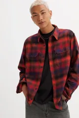 Camisa de franela a cuadros rojos, negros y azules, de corte recto, manga larga, con cuello clásico, cierre frontal con botones, dos bolsillos con solapa abotonada en el pecho y puños abotonados.