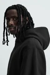 Sudadera tipo hoodie de color blanco hueso, con capucha, manga larga y bolsillo canguro frontal. Presenta un calce relajado y tejido de algodón con interior afelpado.