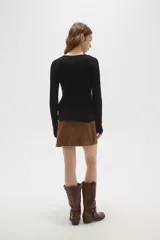 Remera de algodón de calce ajustado, con cuello redondo y manga larga. Presenta una hilera de botones decorativos dorados en el hombro y lateral derecho.