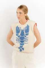 Chaleco tejido a mano en lana merino, color beige con diseño de langosta en color azul y detalles de terminación en rojo en cuello y sisas.