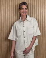 Sobrecamisa de denim soft color beige, de corte oversize, con mangas cortas, bolsillos frontales con solapa, cuello clásico y costuras pespunteadas en contraste.