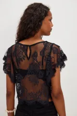 Top corto blanco confeccionado en encaje de nailon con diseño floral transparente, escote redondo y mangas cortas holgadas con terminación festoneada.