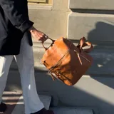 Mochila de eco cuero color suela, de diseño amplio con múltiples bolsillos externos con cierre y tiradores largos. Cuenta con asa superior y correas ajustables.