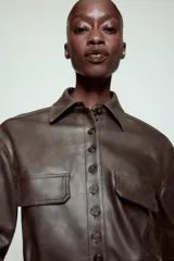 Cazadora de efecto piel con cuello solapa, manga larga y cierre frontal con botones. Presenta falsos bolsillos con solapa en el delantero y bajo con acabado peplum.