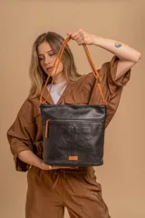 Bandolera mediana de cuero sintético negro con detalles en color naranja. Presenta un bolsillo frontal con cierre, correa regulable y logo de la marca en una etiqueta naranja en la parte inferior.