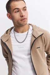 Campera con capucha y cierre frontal, color beige, con detalles de costuras y cierres en negro. Presenta mangas largas con puños acanalados y logo pequeño en el pecho.