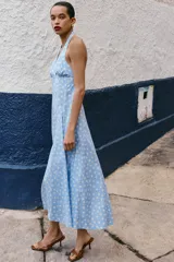 Vestido midi de algodón con estampado de lunares blancos sobre fondo celeste. Presenta cuello halter con cierre de botones y espalda descubierta, con un corte evasé fluido.