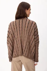 Sweater de punto con diseño de trenzas verticales, cuello redondo y corte crop. Presenta una combinación de colores crudo y camel, con mangas largas y ajuste holgado.