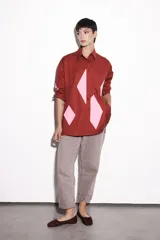 Camisa color bordó de corte recto, con cuello clásico, cierre con botones y mangas largas. Presenta apliques geométricos en color rosa en el frente y los codos.