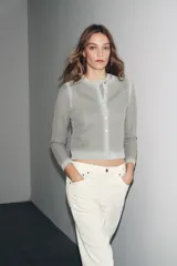 Chaqueta de punto de manga larga y cuello redondo, color gris claro con un sutil brillo metálico y efecto degradado en el tejido. Cierre frontal con botones plateados.