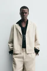 Sobrecamisa de hombre color beige claro, con cuello de solapas de pico, manga larga y cierre frontal de botonadura. Presenta bolsillos de vivo en la cadera.