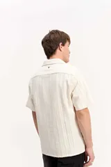 Camisa de manga corta color beige con tejido calado de líneas verticales y cuello abierto estilo resort.