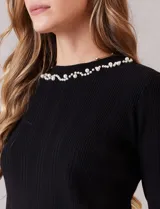 Buzo de tejido soft color negro, con cuello a la base y mangas largas. Presenta apliques de perlas decorativas en el contorno del cuello y en los puños.