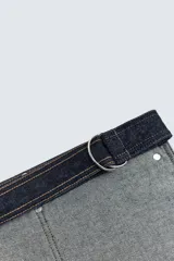 Cinturón tipo utility confeccionado en denim de algodón color azul oscuro con efecto lavado. Presenta un diseño con múltiples bolsillos frontales funcionales, remaches metálicos y ajuste mediante correa con hebillas de doble anilla.