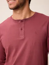 Remera de manga larga con cuello redondo y cierre frontal parcial con botones. Presenta un diseño de color sólido con un pequeño logo bordado en el pecho.