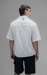 Camisa oversize blanca de manga corta y cuello abierto, confeccionada en algodón con diseño bordado.