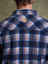 Sobrecamisa de tejido polar con estampado abstracto en tonos rojizos y azul marino. Presenta cuello clásico, cierre frontal con botones a presión, dos bolsillos frontales con solapa en el pecho y un parche decorativo.