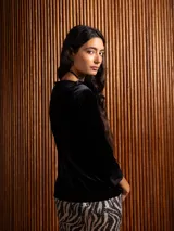 Blusa de terciopelo negro con escote bote y mangas tres cuartos con puños de tela lisa. Presenta un corte al cuerpo y un diseño minimalista.