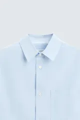 Camisa de manga larga color celeste claro, corte regular fit, con cuello solapa, bolsillo plastrón en el pecho y cierre frontal de botonadura.