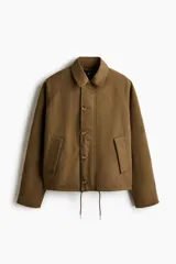 Campera de sarga levemente acolchada con cuello inglés, cierre frontal y solapa con botones. Presenta mangas raglán, bolsillos insertados delanteros y cordón ajustable en el bajo.