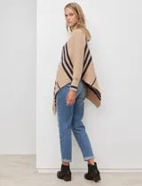Poncho de tejido color beige con cuello alto y rayas diagonales anchas en azul marino. Presenta mangas largas y terminación asimétrica.