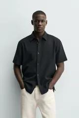 Camisa regular fit negra de manga corta, con cuello bowling y cierre frontal de botonadura. Confeccionada en tejido texturizado con elasticidad y aberturas laterales en el bajo.