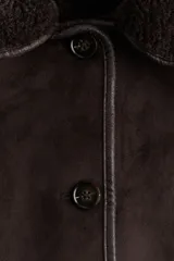 Campera oversized de doble faz con exterior de efecto gamuzado y forro interior de sherpa. Presenta cuello clásico, cierre frontal con botones, hombros caídos y bolsillos laterales insertados.