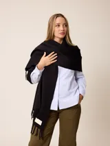 Pashmina de textura suave y color crema, con diseño liso y terminaciones en flecos en los extremos. Incluye una etiqueta decorativa en una de las esquinas.