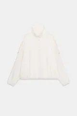 Chaqueta oversize color crudo, con cuello subido, manga larga con puños elásticos y bajo abullonado. Presenta cierre frontal con botones a presión ocultos, bolsillos de vivo en el delantero y trabillas en los hombros.