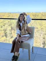 Chaleco tejido de punto con diseño asimétrico, presentando un lado en color marrón oscuro y otro en beige, ambos decorados con motivos geométricos y figuras de llamas bordadas. Posee cierre frontal con cordones de cuero y terminaciones en tejido elástico con franjas decorativas.