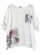 Blusa blanca de lino, con cuello redondo, mangas tres cuartos con trabilla y botón, bolsillo superior y apliques de tela estampada con flores en violeta y verde.