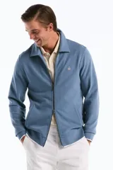Campera de punto azul con cierre frontal completo, cuello tipo camisa y bolsillos ribeteados, decorada con el logo del pingüino bordado en el pecho.