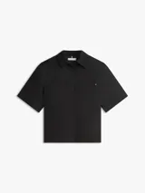Camisa de manga corta de corte amplio confeccionada en puro lino, de color negro, con cuello inglés y un bolsillo de parche en el pecho que incluye un sutil logo bordado. Presenta hombros ligeramente caídos y cierre frontal de botones.