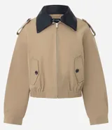 Campera Comfort de poliéster color camel, con cuello de poliuretano en contraste color marrón oscuro, cierre frontal y bolsillos con solapa y botones. Presenta martingalas en los hombros y elástico en la cintura.