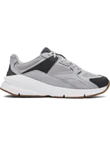 Championes Under Armour modelo Forge 96 Reissue, con diseño inspirado en los años 90. Presenta una parte superior combinada de malla y cuero nobuk en tonos gris y negro, con refuerzos de TPU. Incluye una entresuela blanca de amortiguación y suela exterior de goma en color caramelo.